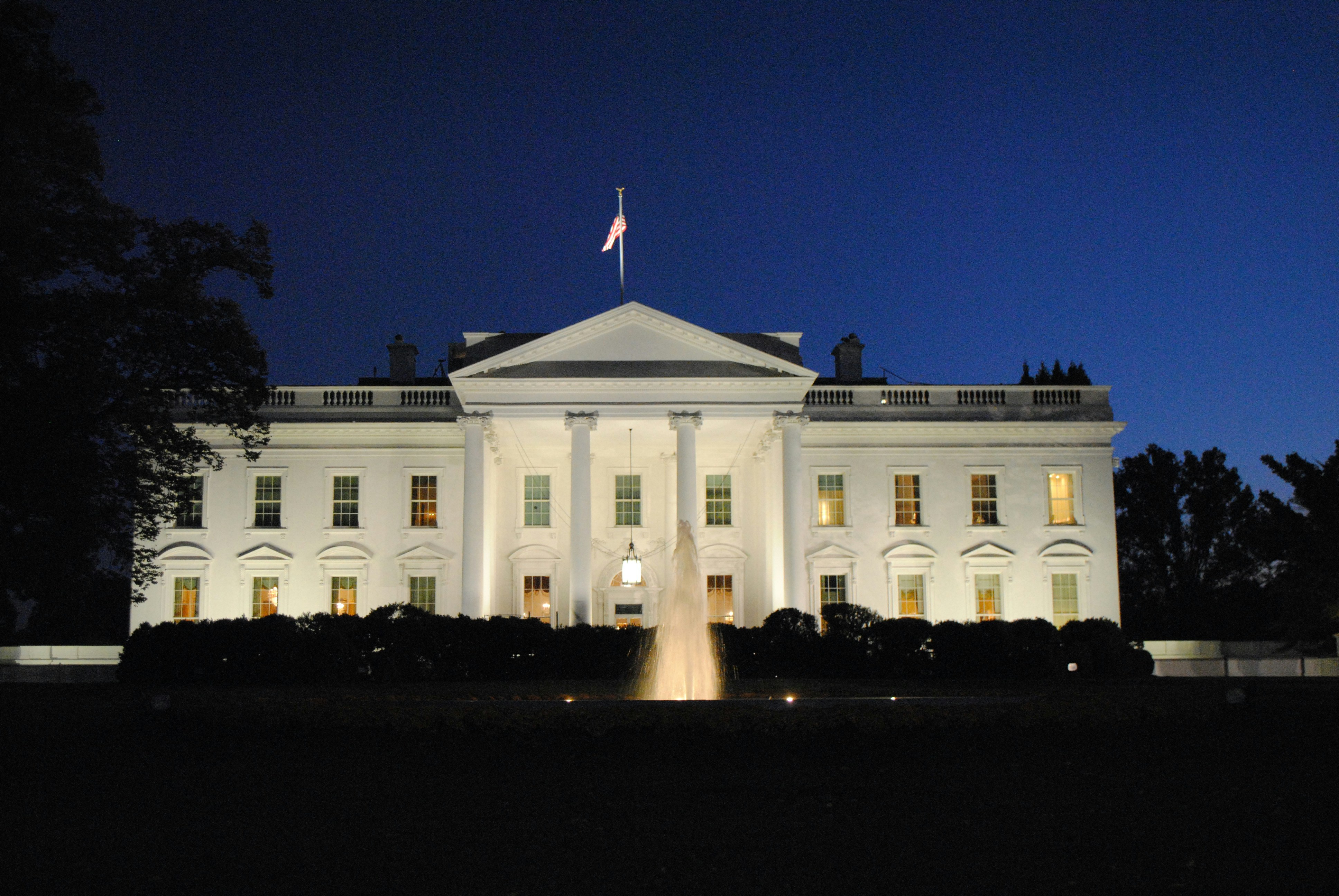 Front view of the White House at night, fully illuminated, with a dark sky in the background.
