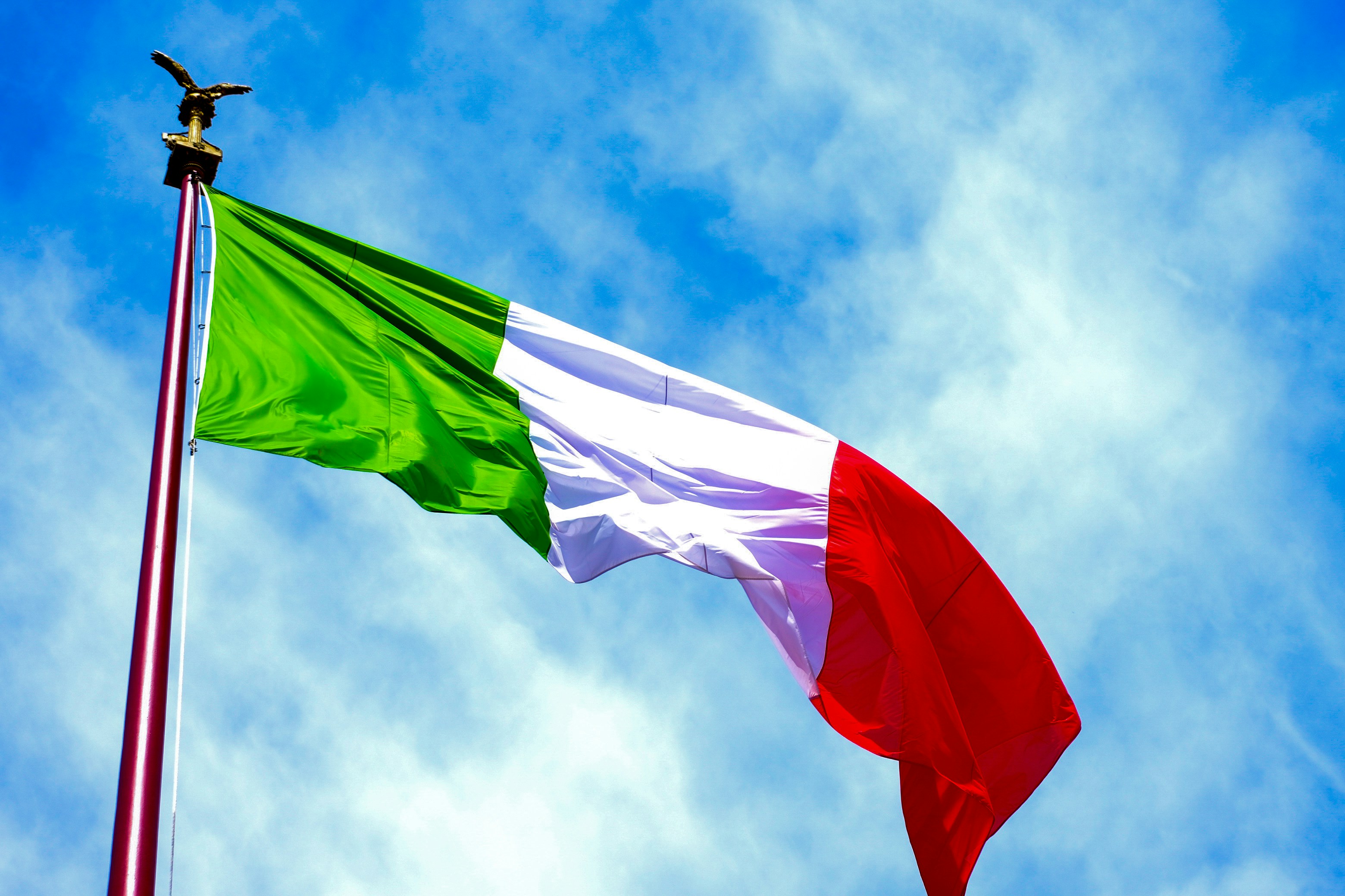 The Italian flag waving against a clear blue sky.