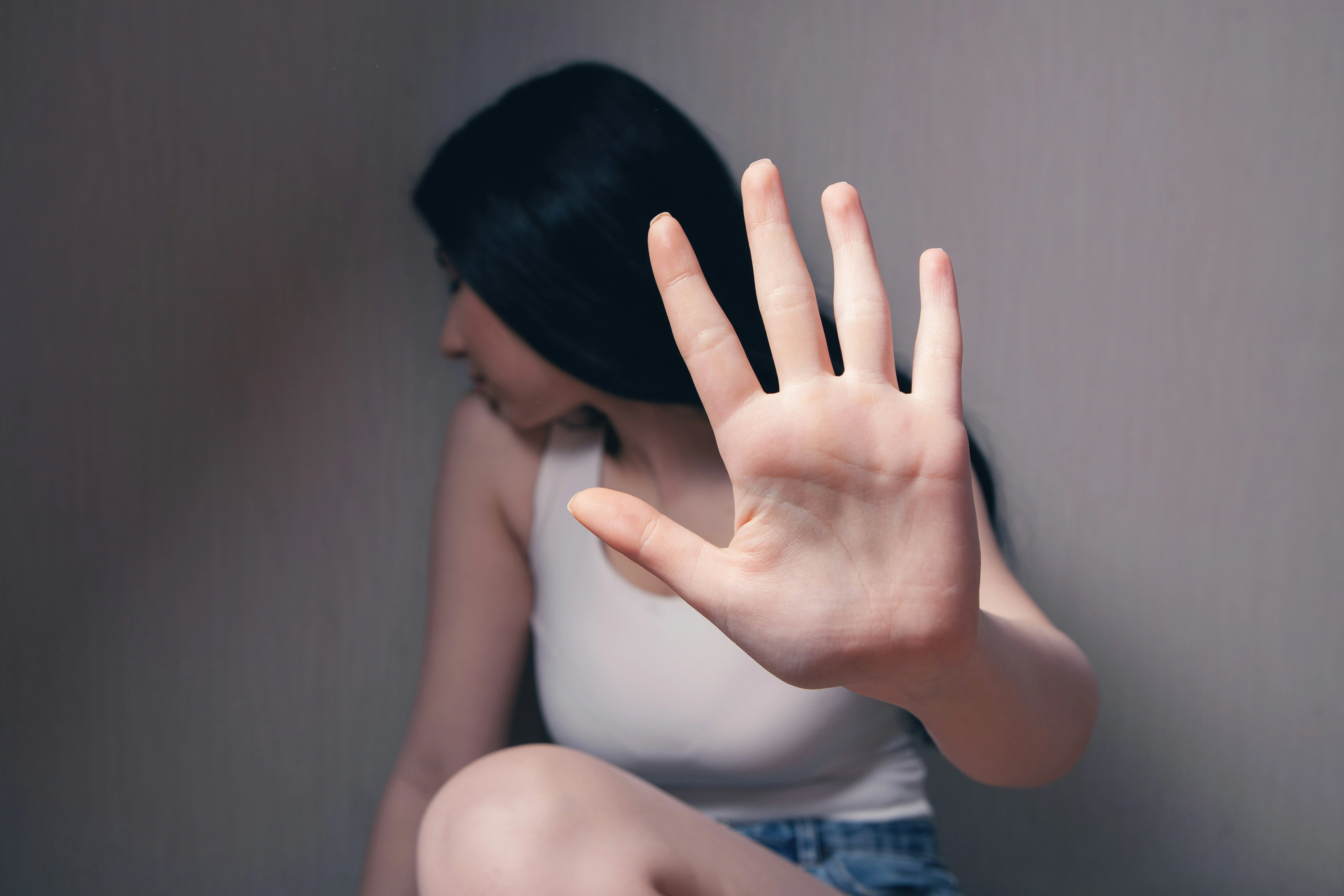 Woman in white tank top covering face with her hands.
