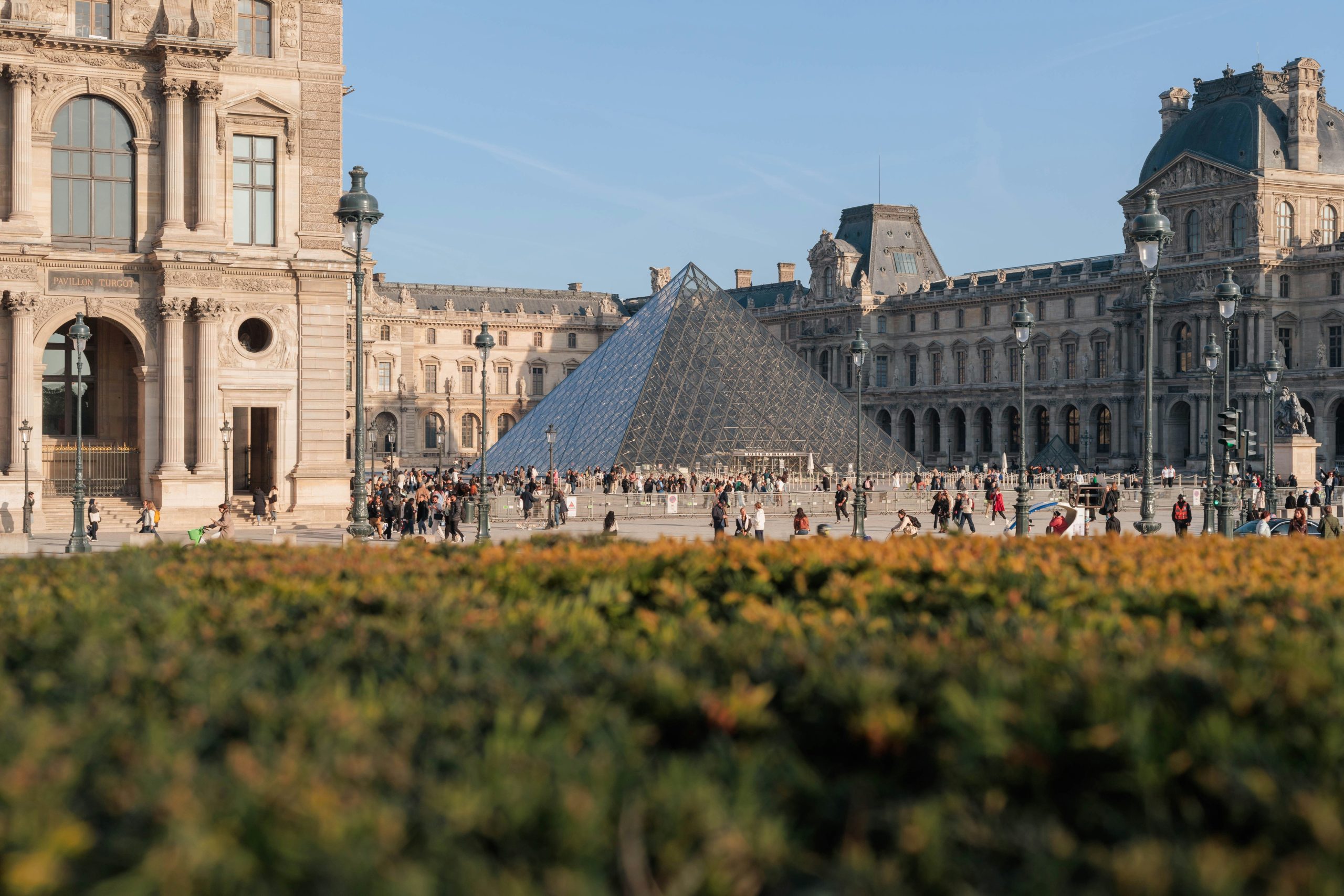Louvre Museum with glass pyramid and gardens on a sunny day with people gathering.