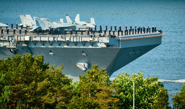 A large Navy ship with fighter jets on top.