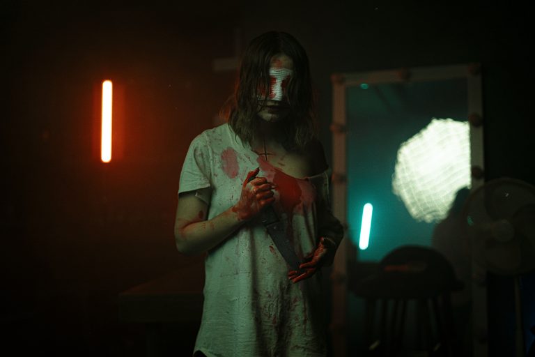 A man holds a knife in a horror scene.