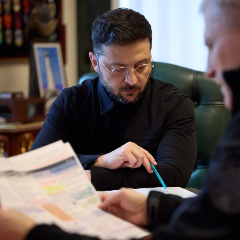 President Zelenskiy reviewing papers with a pen in hand, seated near Oleh Ivashchenko, who also looks at the documents.