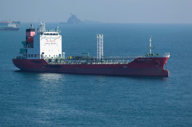 A red tanker vessel sails across the sea, with no land visible on the horizon.