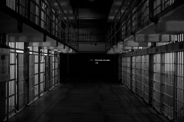 Empty, dimly lit prisoner cells with shadows casting a gloomy atmosphere.
