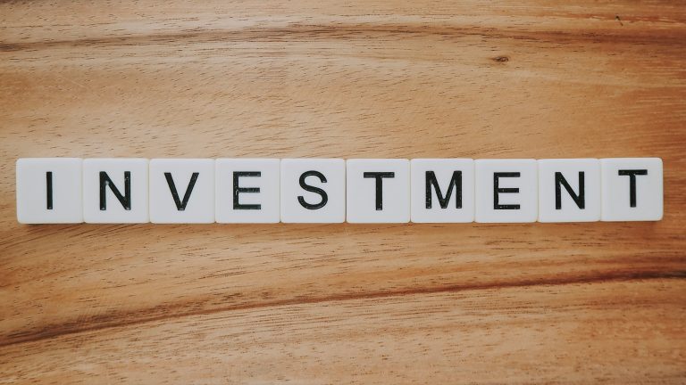 The word 'INVESTMENT' in capital letters on a wooden table.