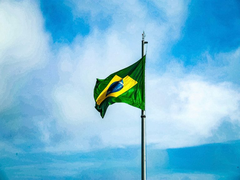 Green and yellow Brazilian flag waving under a clear blue sky.