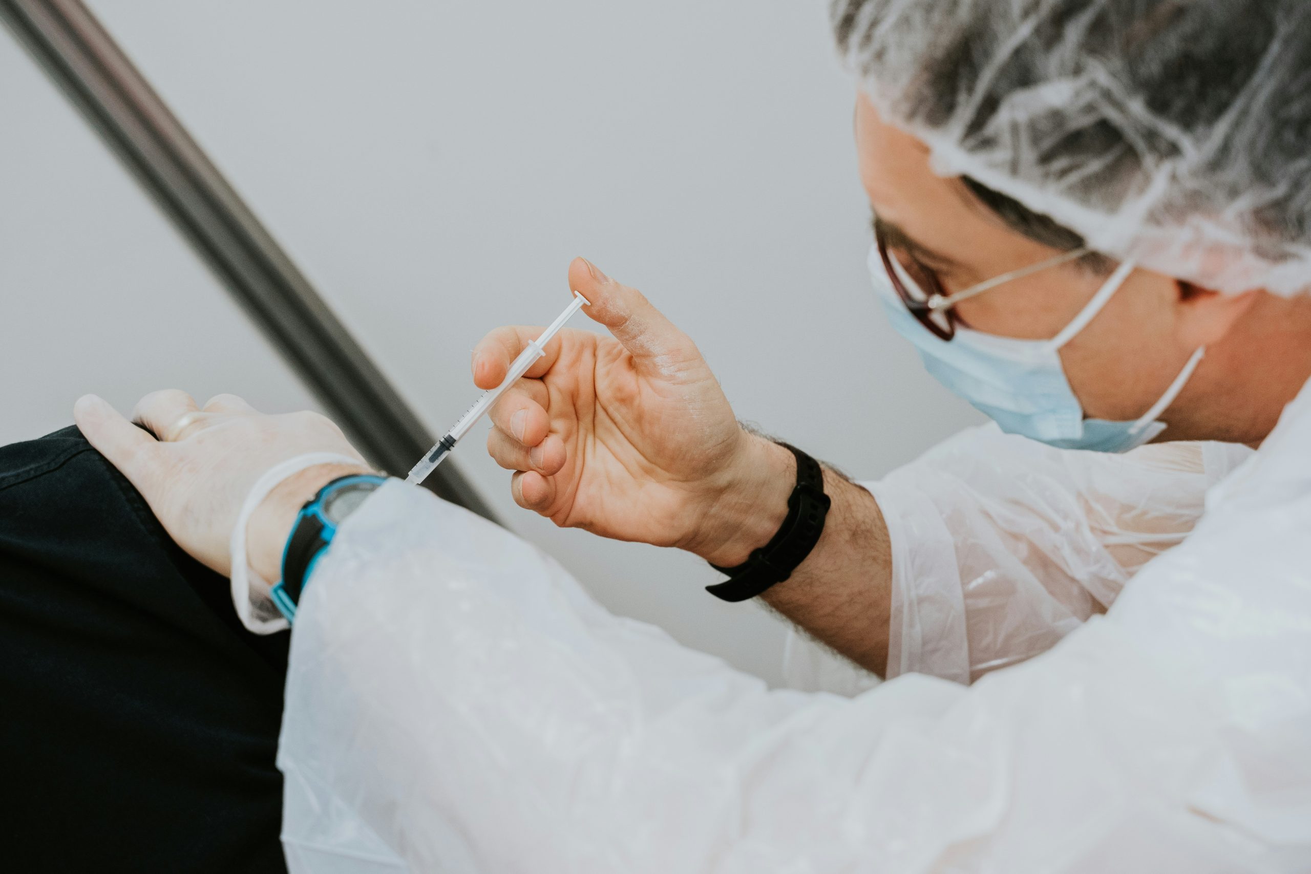 Doctor in a white long-sleeve shirt giving an injection to a patient.