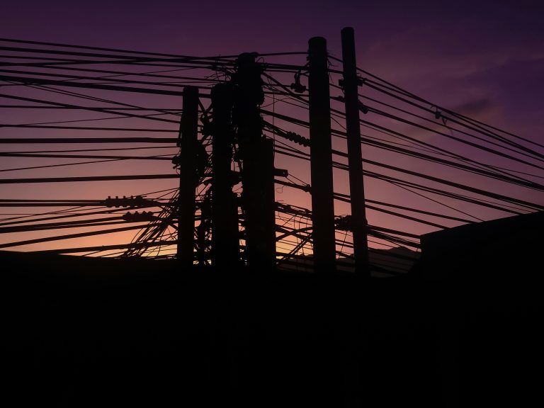 A group of electric poles silhouetted against the evening sky.