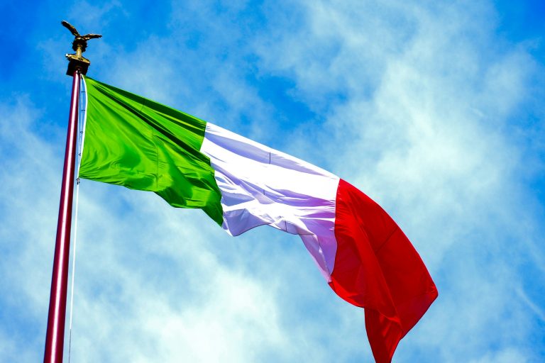 The Italian flag waving against a clear blue sky.