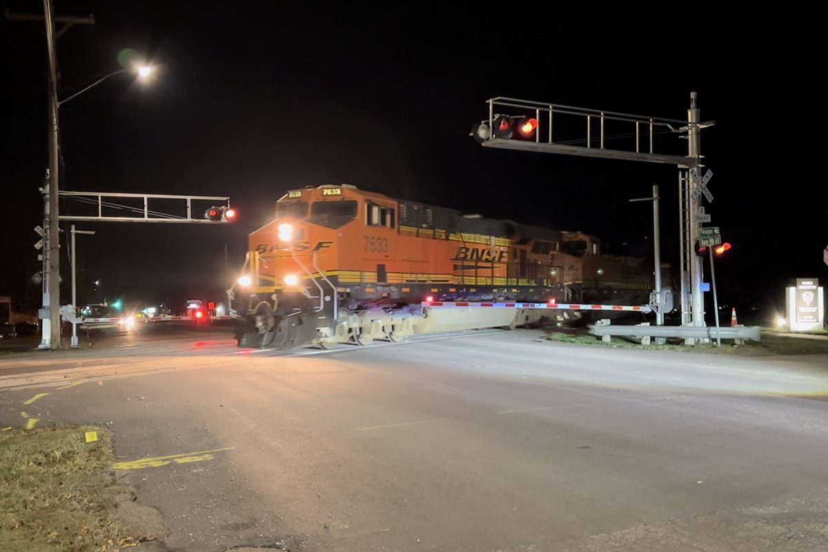 A BNSF locomotive stopped at a railroad crossing with active red lights and lowered crossing arms at night.