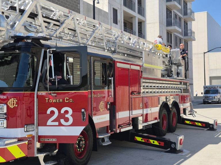 Side view of Chicago Fire Department Tower Company 23, a red E-ONE Cyclone aerial ladder truck with extended stabilizers and fire personnel on the rear platform.