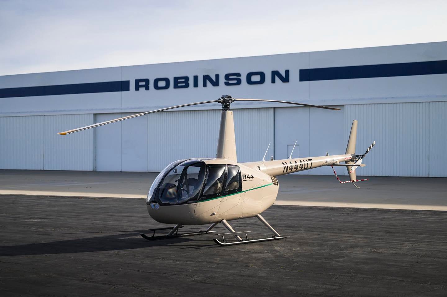 A white Robinson R44 helicopter parked outside a building.