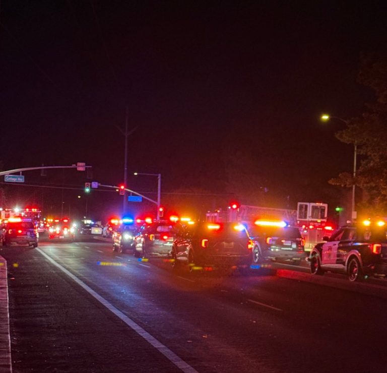 A line of law enforcement and fire department vehicles with flashing red and blue lights illuminated at night on a Sacramento street near Cottage Way.
