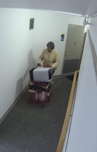 A woman fitting the description of missing person Rosie McMurray is seen from above in a hallway. She is wearing a beige jacket, dark pants, and pushing a wheeled cart with an item on top.