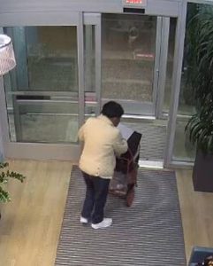 A woman fitting the description of missing person Rosie McMurray is seen from behind leaving a building. She is wearing a beige jacket, dark pants, and pushing a wheeled cart.