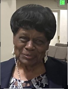 Close-up portrait photograph of Rosie McMurray smiling slightly. She is wearing a blue jacket, patterned top, and dangling earrings.