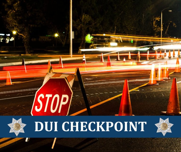 A nighttime long-exposure photo of a DUI checkpoint featuring traffic cones, a stop sign, and a blue banner with the Santa Rosa Police Department badge.