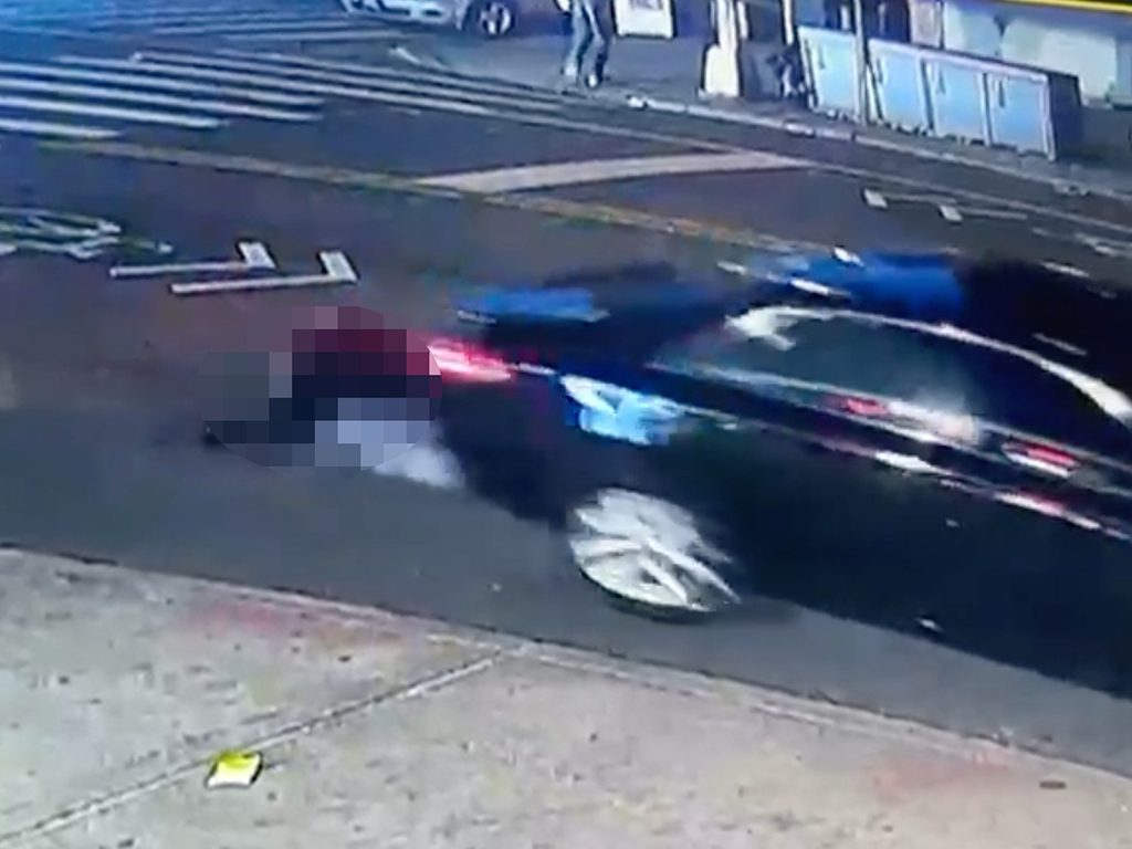 Surveillance still showing a car driving away with a person on the ground near the rear.